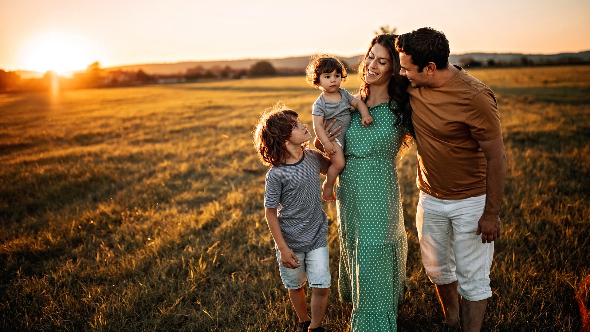 Familie mit zwei Kindern geht bei Sonnenuntergang über eine Wiese